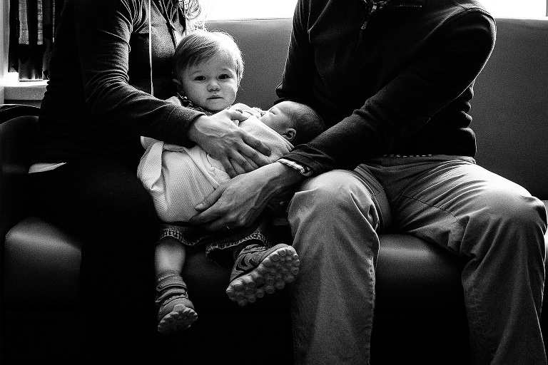Black and white. Mother and father sitting with son and newborn baby in hospital.