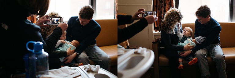 Woman takes picture of father and mother holding toddler and newborn.