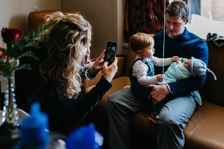 Woman takes picture of father holding toddler and newborn.