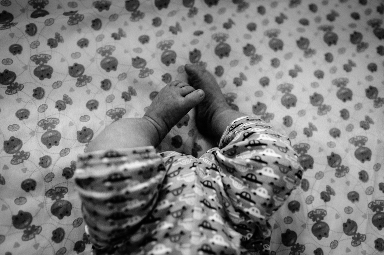 Black and white. Newborn baby's tiny legs curled up and feet laying on a bed