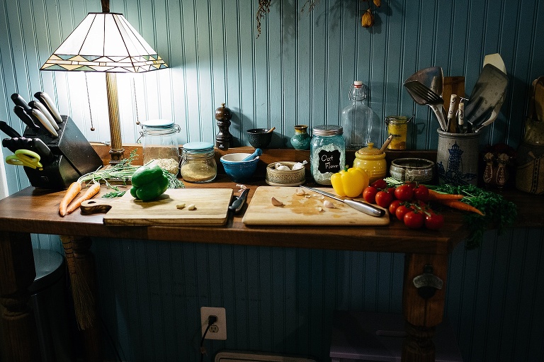 Many fresh vegetables sit on kitchen counter next to two wooden cutting boards.