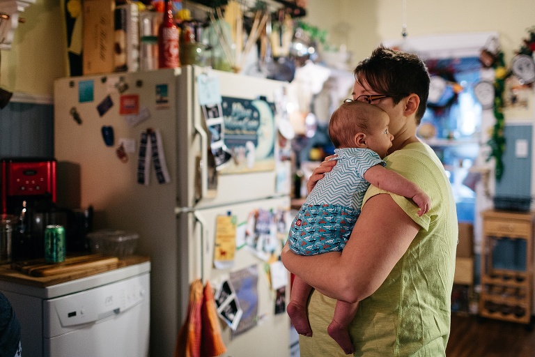 Mother holds newborn son in her kitchen.