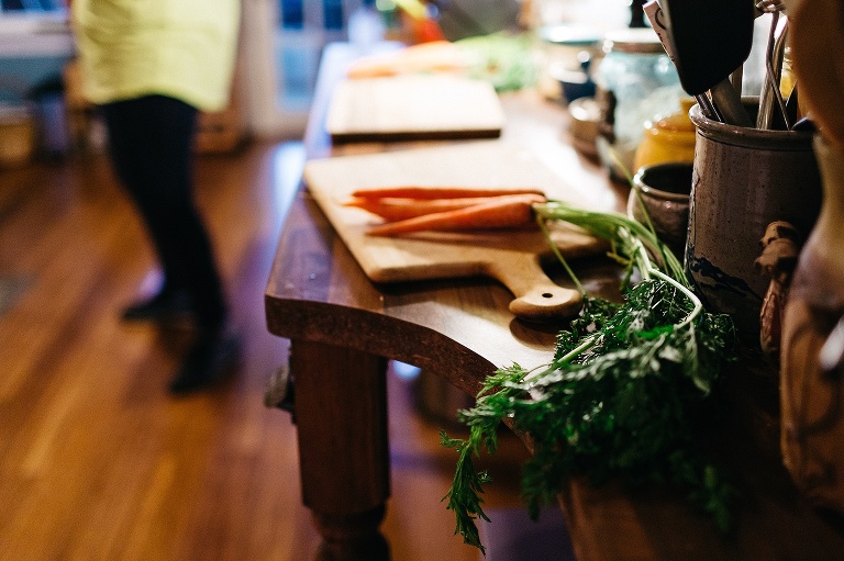 Fresh orange carrots with green leaves still on lay on a wood cutting board on a wood table.