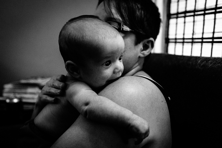 Black and white. Mother holding baby boy as he looks over her shoulders and out the window.