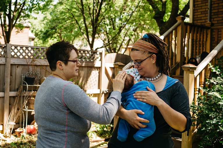 Two mothers in their backyard one holding their sleeping baby boy the other stroking his head.
