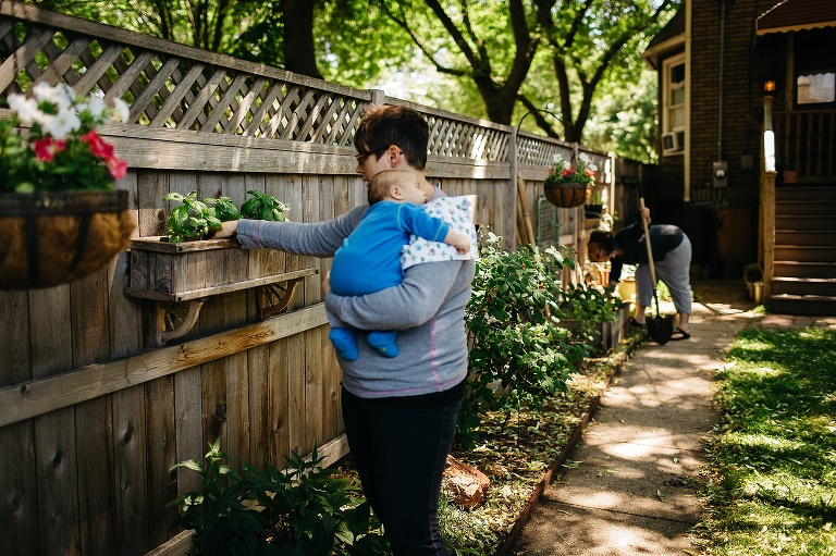 Two mothers gardening in their backyard, one holding their sleeping baby boy.