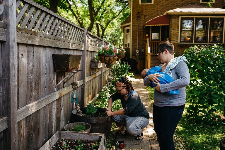 Mother holds sleeping baby boy while watching a women garden in their backyard.