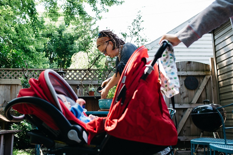 Baby boy laying in a red stroller mother standing on the patio next to him.