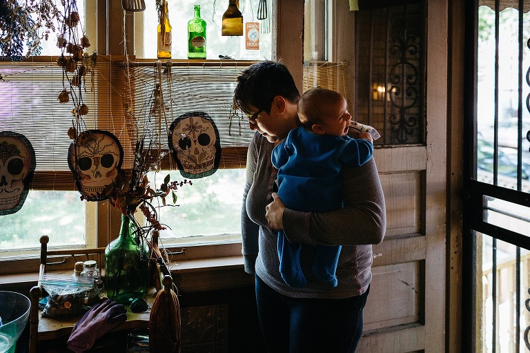 Mother holds her crying newborn son in entry way to a house.