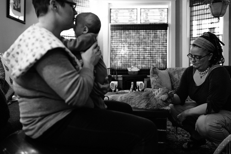 Black and white. Two mothers sit inside holding their newborn son.