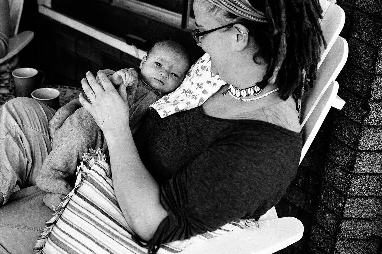 Black and white. Mother holds newborn son while sitting on a patio chair.
