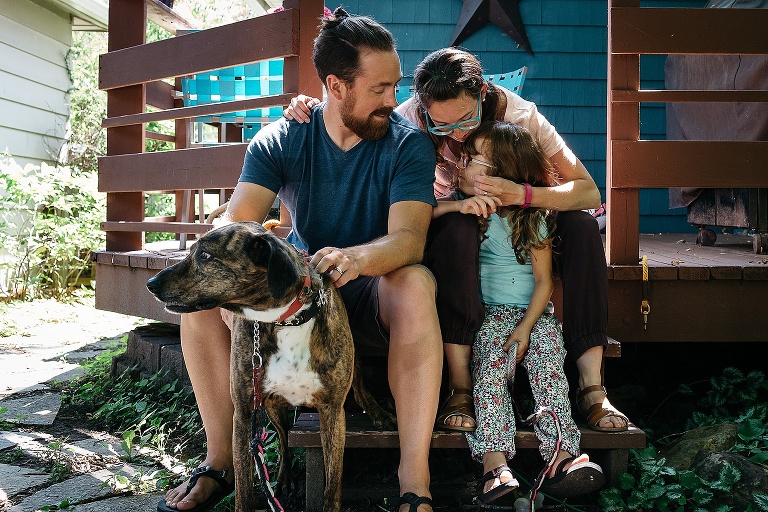 Mother, father, daughter, and the dog sit on backyard porch.