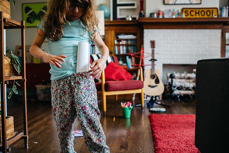 Young girl puts a treasure map rolled up in her pants waistband.