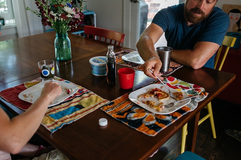 Family sits at kitchen table eating a breakfast of strawberry pancakes and sausages.