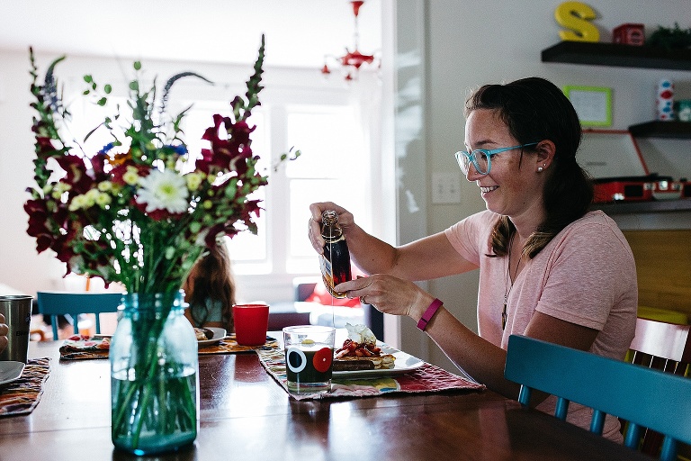 Mother sitting at kitchen table pours syrup onto strawberry pancakes.
