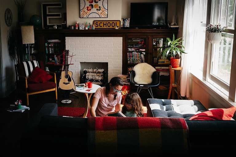 Mother sits with daughter on the living room couch reading books.