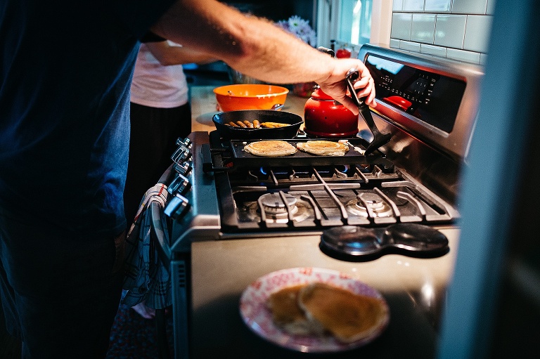 Father flips strawberry pancakes on the stove griddle.