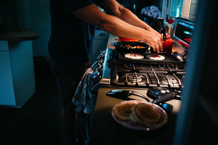 Father makes strawberry pancakes on the kitchen stove griddle.