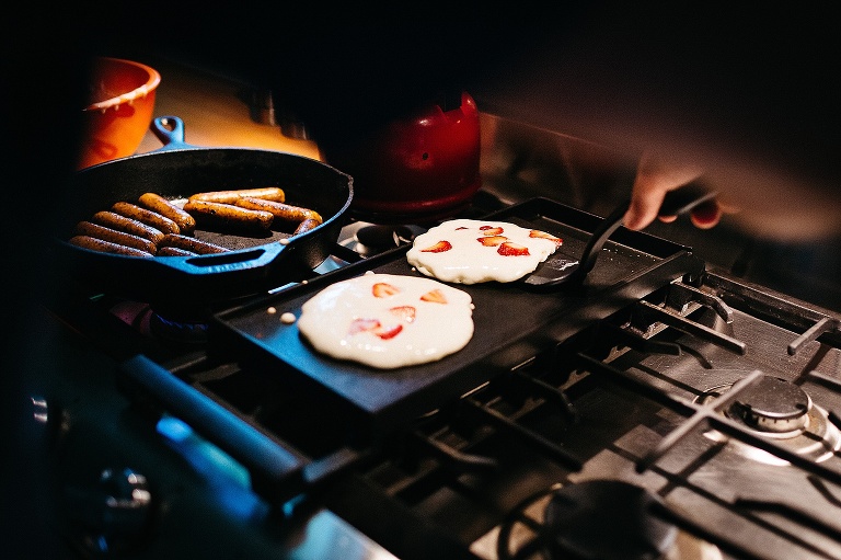 Father flips strawberry pancakes on the stove griddle.