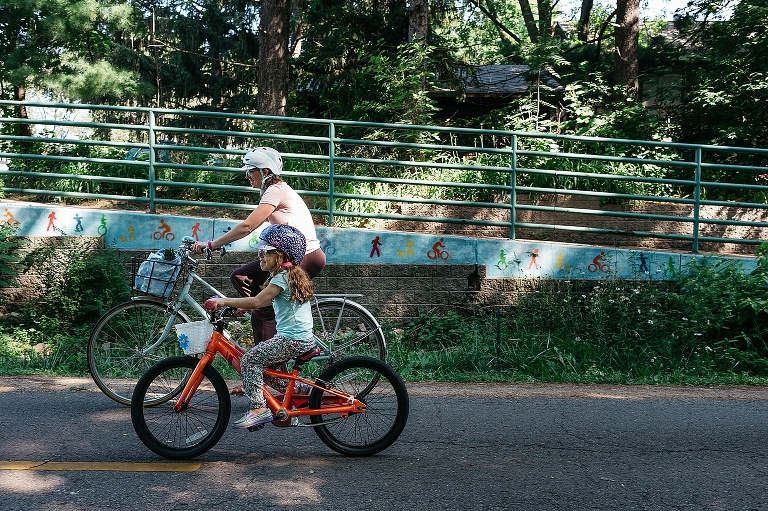Mom and daughter bike on a bike path on their way home from a farmers market.
