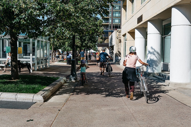 Mother, father, and daughter walk their bikes down a wide sidewalk on their way home.