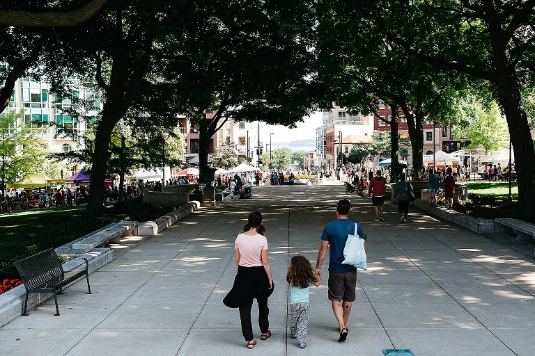 Mother, daughter, and father holds hands as they walk down a path at a farmers market.