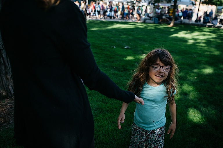 Young girl high fives her mother after playing hide and seek in the grass at a farmers market.