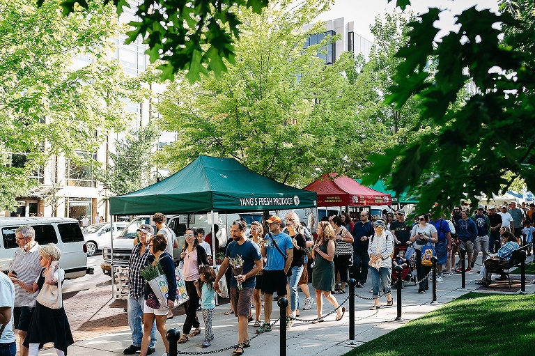 Mother, daughter, and father walk in a crowd of people at a farmers market.