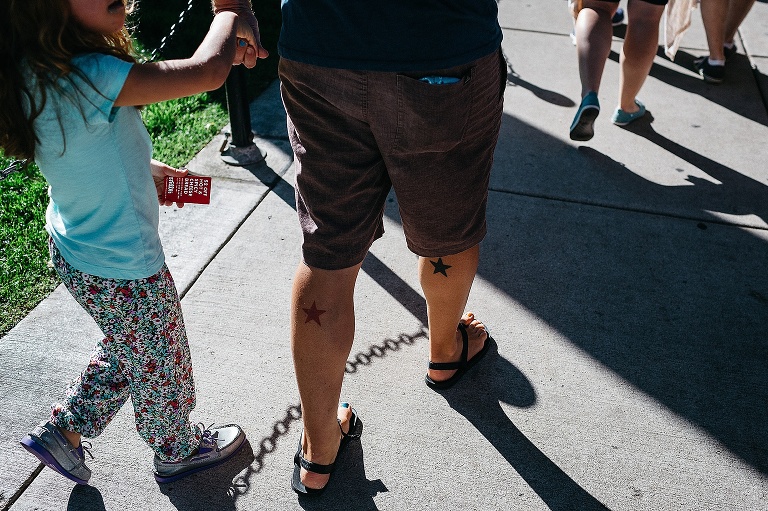 Father holds daughters hand while walking at a farmers market.