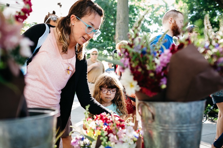 Mother stands with daughter at a farmers market picking out a bouquet of flowers.
