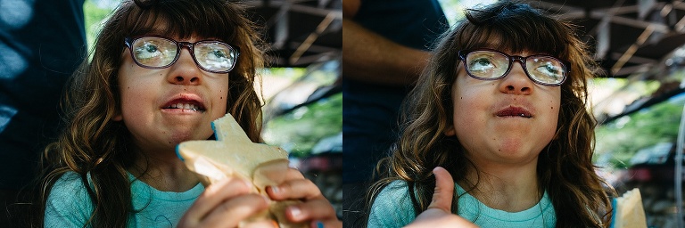 Young girl eating a blue star cookie gives a thumbs up.