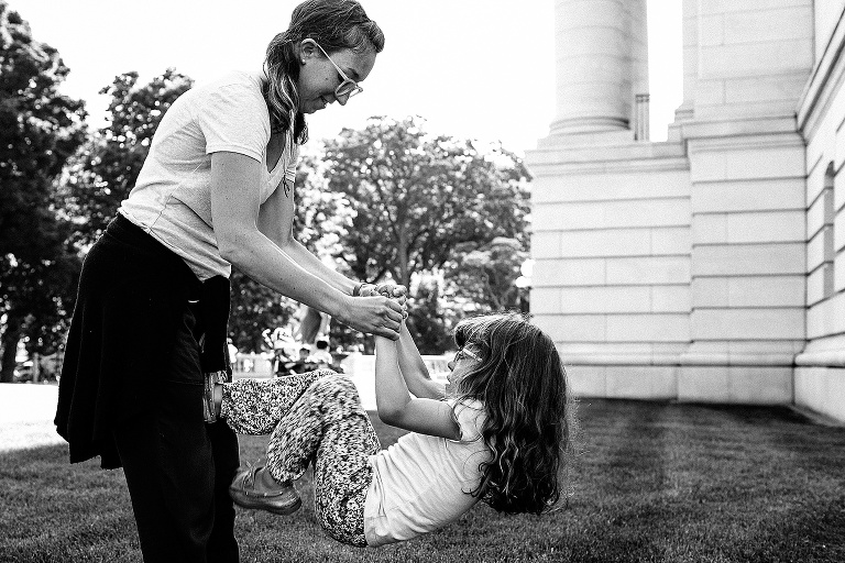 Black and white. Mom holds daughters hands as daughter climbs up her mothers legs.