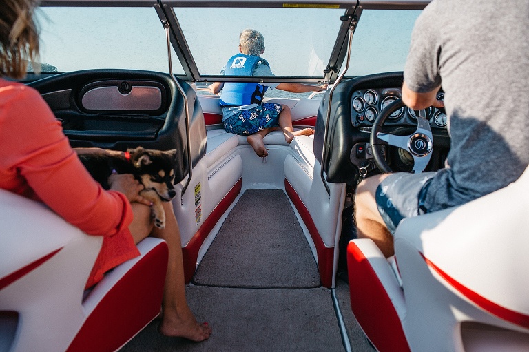 Father driving a boat, mother sitting next to him with a puppy on her lap, son sitting in the front of the boat looking ahead.