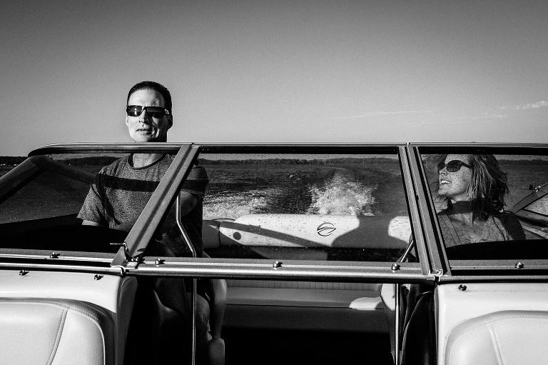 Black and white. Man driving a speed boat, wife sitting next to him.