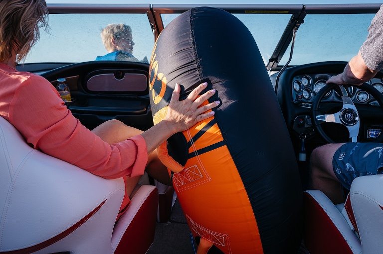 Dad driving a boat, mom holding a inter tube, son sitting up front.