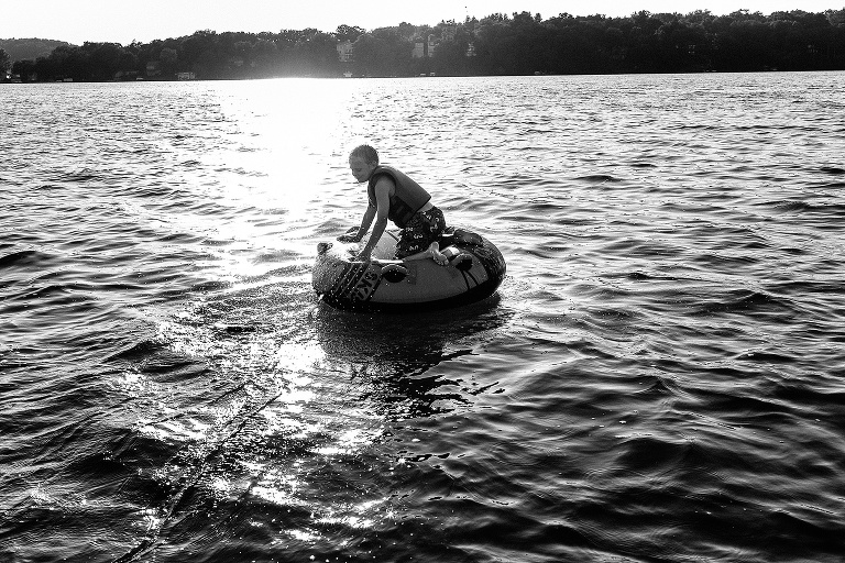 Black and white. Kid sitting on inter tube on the lake after going tubing from motorboat.