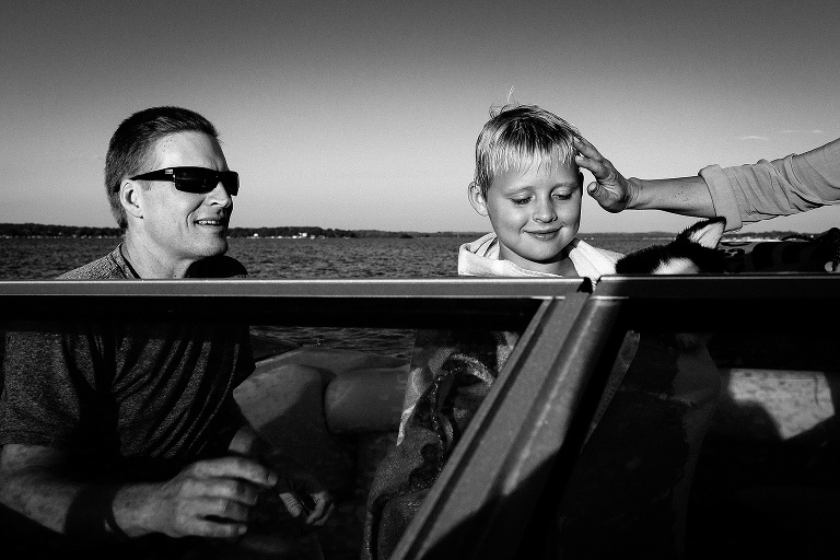 Black and white. Father, mother, and son on their motor boat. Mother fixes boys hair after he went tubing on the lake.