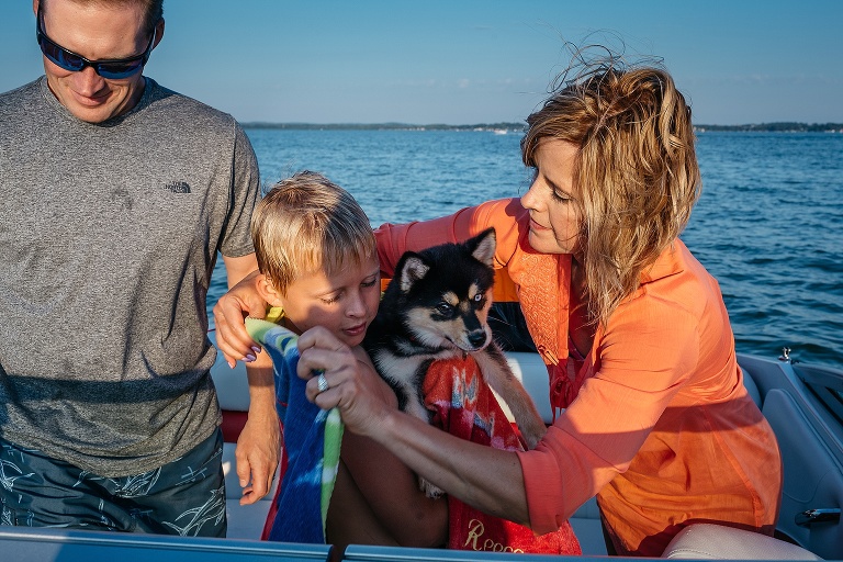 Mother, father and son on their motorboat, son wrapped in a towel holds puppy.