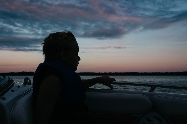 Shadow of a boy sitting on a boat looking at the end of the sunset.