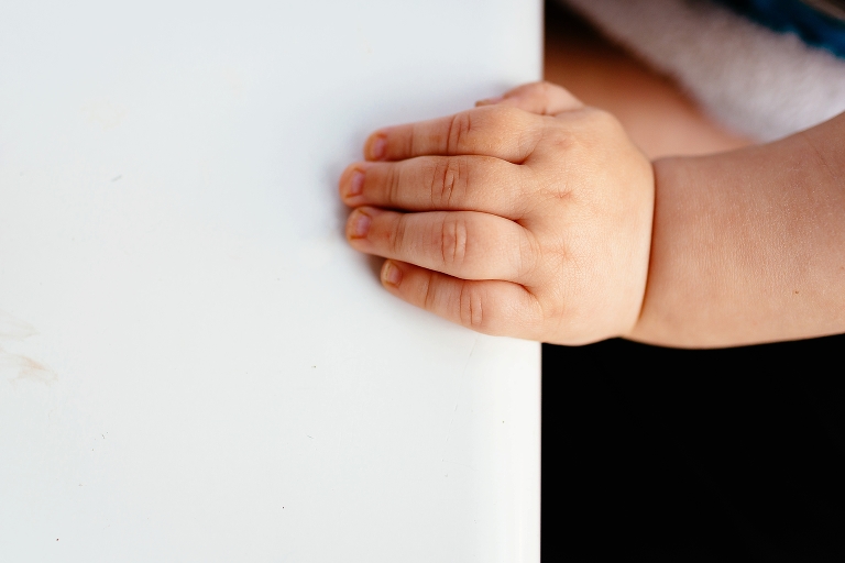 baby little hand holds onto white table.