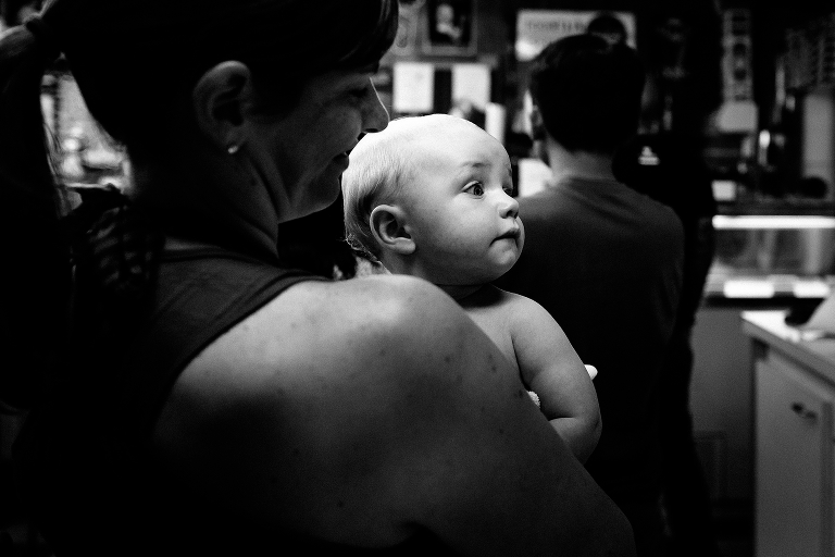 Black and white. Mother holds baby son as she stands in line for ice cream.