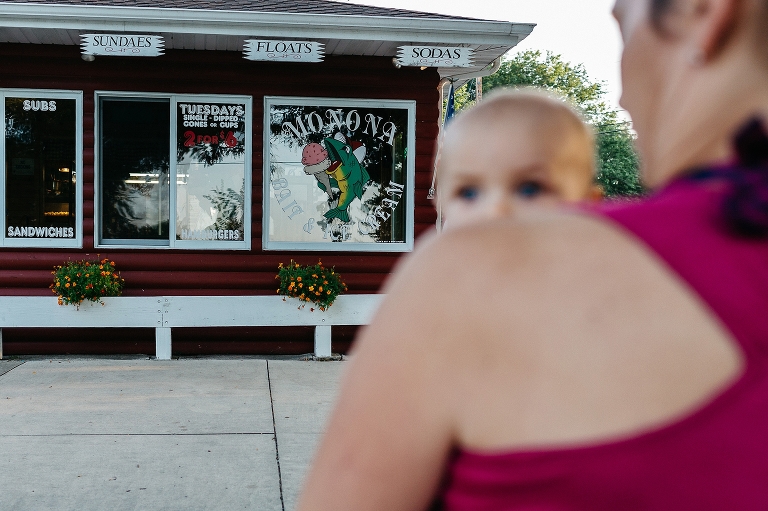 Mother holds baby boy as she walks up to a local ice cream shop.