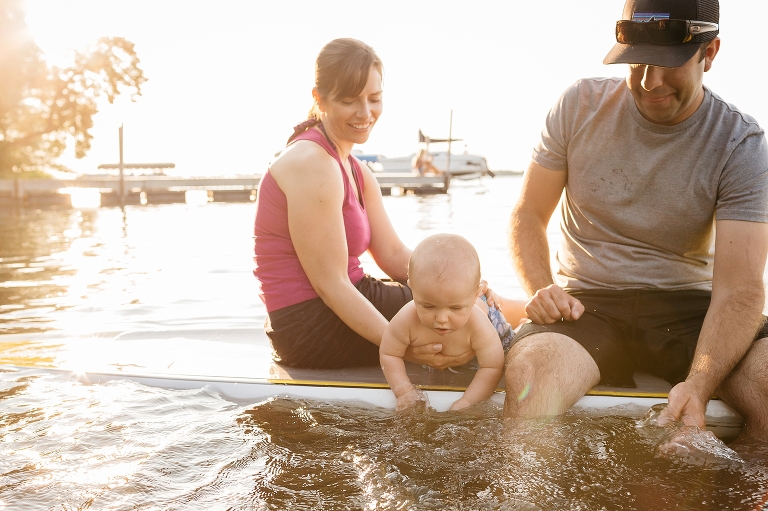 Mother and father sit on a SUP holding onto baby son 