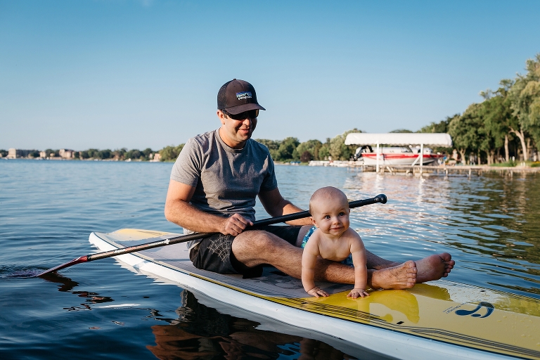 Father and baby son siting on a SUP in the lake.
