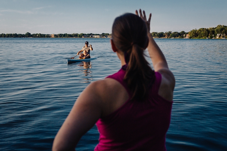 Mom waving to her husband and son sitting on a stand up paddle board in the lake.