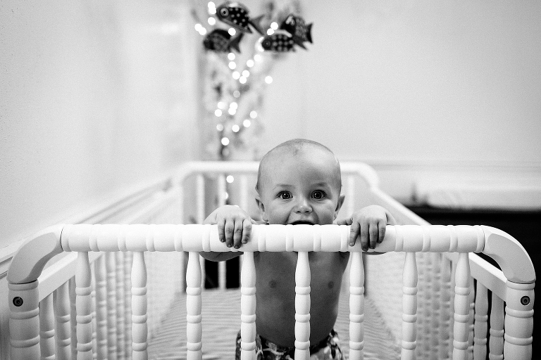 Black and white. Baby standing in his crib looking at the camera.