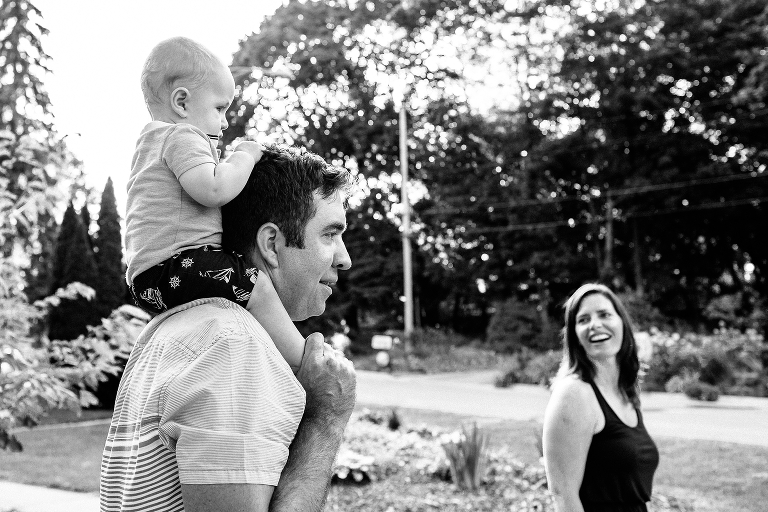 Black and white. Family walking outside Dad holding baby on his shoulders mom walking next to them.