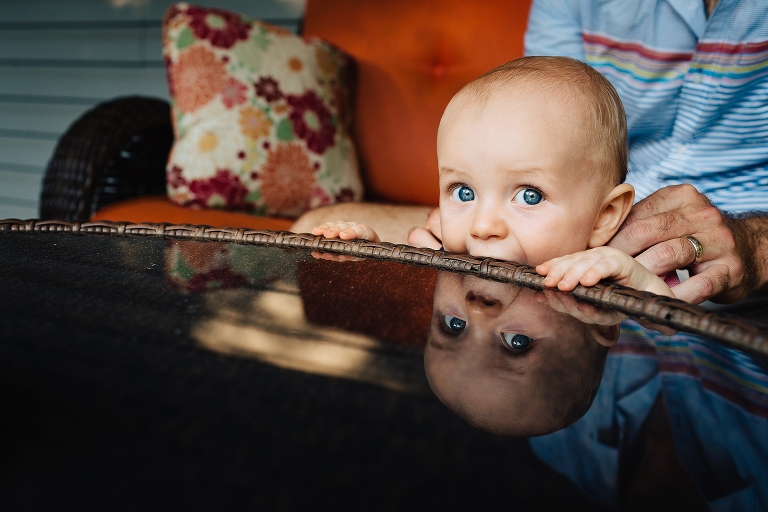 Baby bites patio table looking at camera.