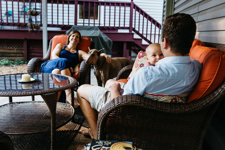 Family sitting on backyard patio. Father holding baby son, mother petting the dog.