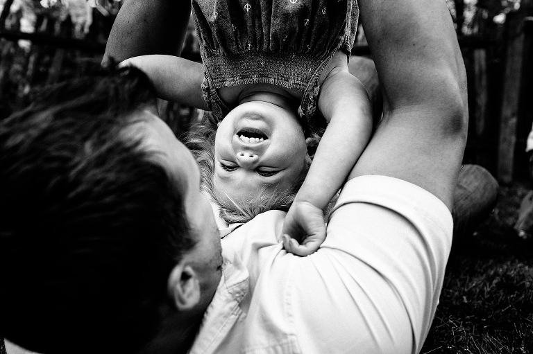 Black and white. Father holds laughing daughter upside down